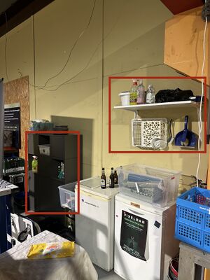 An image showing a cupboard, mini fridges with a shelf above them. The cupboard and shelf are outlines with a red rectangle indicating where the cleaning supplies live